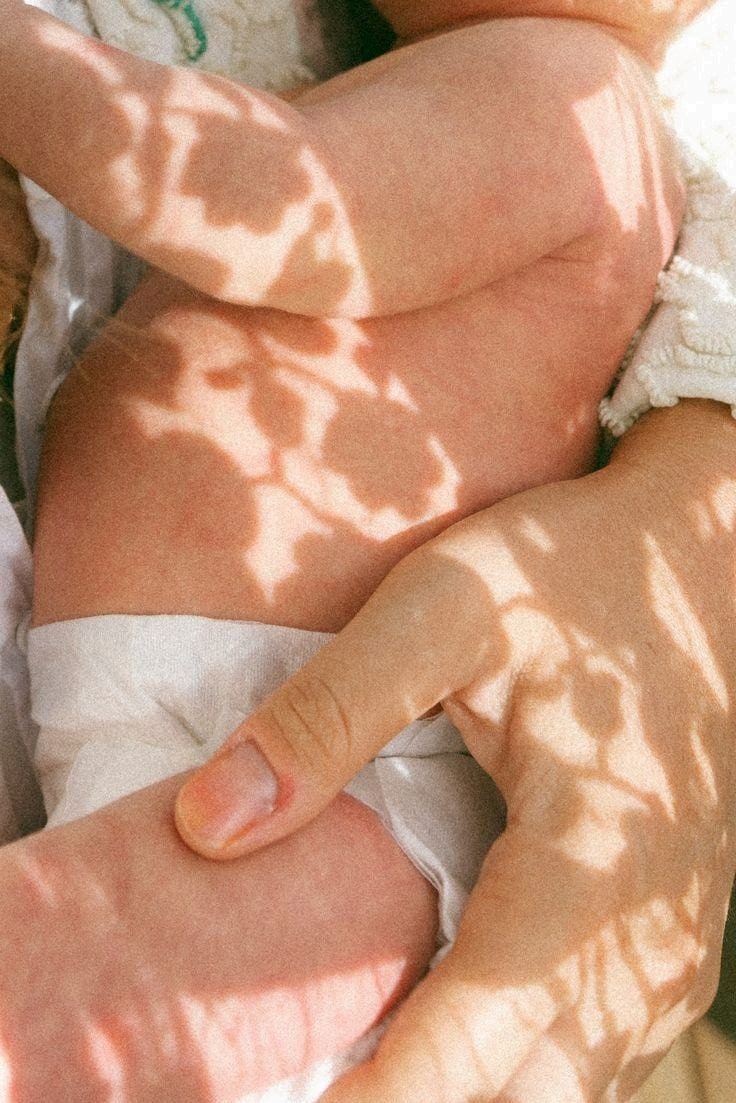 A mother's hand resting on her baby, dappled in soft light